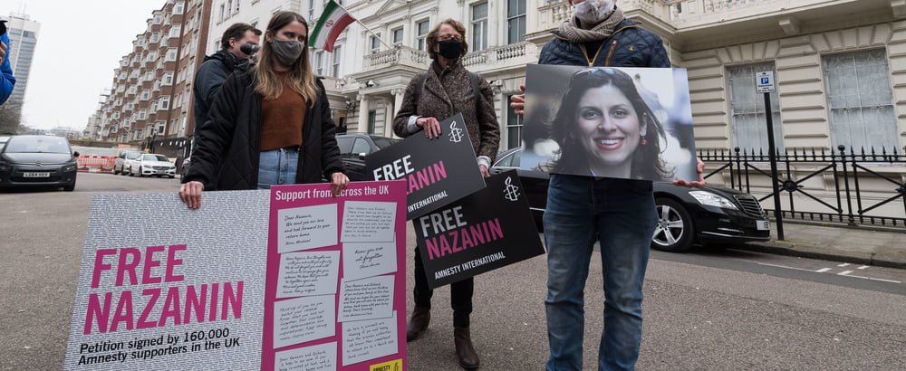 Group of four protestors in the middle of the road holding Nazanin's portrait and cards that read 'Free Nazanin'. 